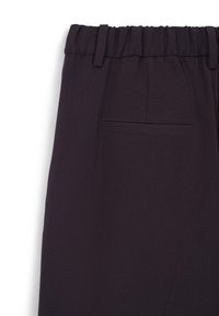 Détail d’un pantalon noir à taille élastique avec passants de ceinture et une poche arrière passepoilée sur un tissu lisse.