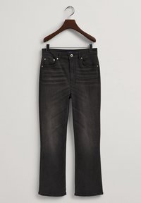 Jeans de mezclilla negra en una percha de madera. Diseño de pierna recta con bolsillos frontales y detalles de costura visibles. Textura suave, desvanecimiento mínimo.