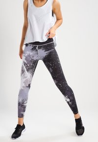 Leggings noirs avec un motif éclaboussé abstrait blanc et gris, associés à un débardeur léger gris clair. Tissu texturé et design athlétique.