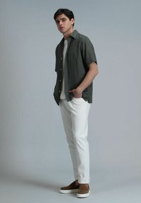 Korte mouwen, donkergroene shirt met knopen, gecombineerd met witte broeken en bruine instappers. Gladde textuur, casual pasvorm.