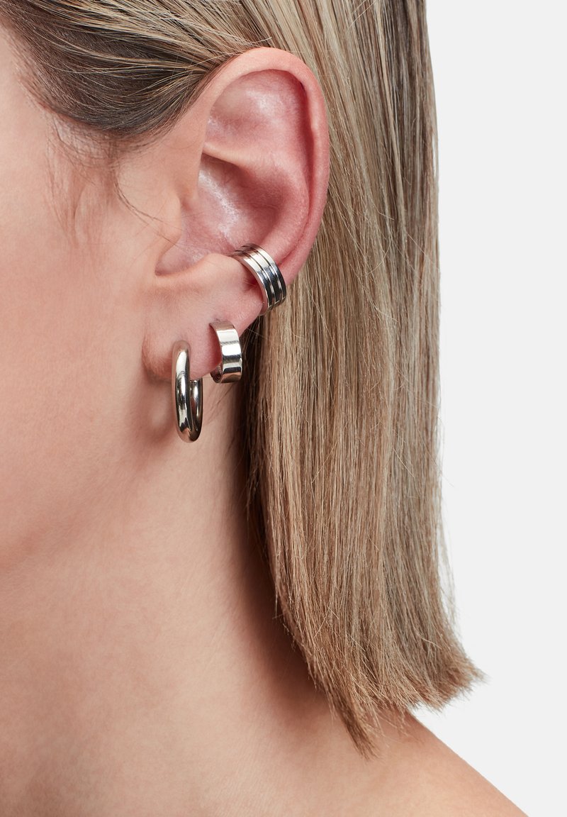 Zilveren creolen tentoongesteld aan een doorboord oor, met verschillende vormen: één glad, één met een getextureerde band, beide weerkaatsend licht.