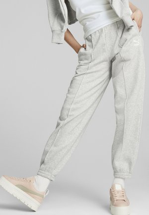 Personne portant un pantalon de survêtement Puma gris clair, des chaussettes blanches, des baskets à plateforme rose pâle et un sweat à capuche gris noué autour des épaules.