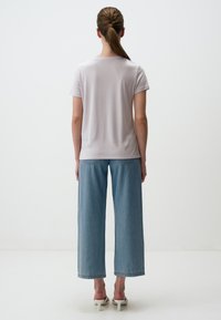 Lichtgrijze T-shirt met korte mouwen gecombineerd met lichtblauwe wijde jeans; heeft een eenvoudig ontwerp en een zachte textuur. Witte hakken maken de look compleet.