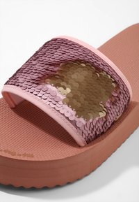 Sandale mule rose avec semelle texturée et bride recouverte de sequins réversibles roses et dorés.