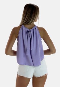 Lila haltertop van lichtgewicht stof, met een geraffineerde halslijn en een strikdetail aan de achterkant, gecombineerd met witte shorts.
