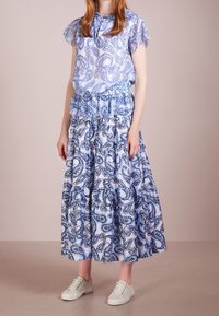 Robe bleu à motif cachemire avec un haut péplum à volants, manches courtes et jupe fluide ; associée à des baskets blanches.