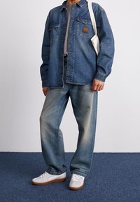 Jeansskjorta i medelblått med två bröstfickor och en fyrkantig etikett; ihop med ljusblå, löst sittande jeans och vita sneakers.