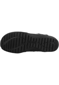 Suela de zapato negra con superficie de goma texturizada, que presenta surcos para proporcionar tracción y un logo grabado en el centro.