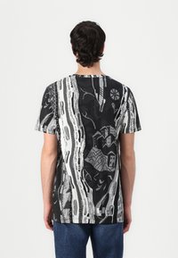 Grafisk T-skjorte med et svart og hvitt abstrakt design med hus og linjer, laget av et lett stoff, med korte ermer og rund hals.