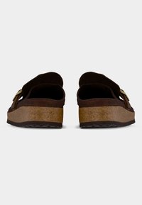 Ζευγάρι καφέ σουεντ κλογκς με φερμουάρ από φελλό στη σόλα και ρυθμιζόμενα λουράκια με χρυσή αγκράφα, εμφανιζόμενα από πίσω.