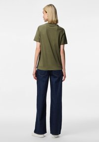 Olivengrønn bomulls t-skjorte med korte ermer, avslappet passform. Kombinert med høytlivs mørk denimjeans. Modellens rygg er synlig.