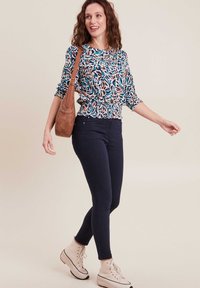 Top a fantasia colorata con vita arricciata, abbinato a jeans skinny scuri e stivaletti crema, portando una borsa a tracolla marrone.