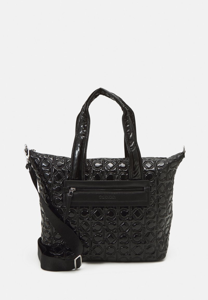 Sac fourre-tout noir brillant avec motif en relief du logo CK répété, deux poignées, poche à fermeture éclair à l'avant, et sangle d'épaule réglable.