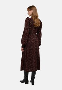 Robe longue à manches longues noire à fleurs avec des accents froncés, taille cintrée et silhouette fluide, associée à des bottes noires jusqu'aux genoux.