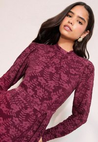 Bordo kleita ar garām piedurknēm, kurai ir teksturēts ziedu raksts. Pabeigta ar augstu apkakli un izceltu vidukli. Eleganta dizaina detaļas.