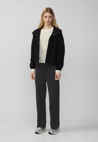 Veste noire courte avec capuche, pull léger en tricot, pantalon gris foncé et chaussures de sport en argent. Tissu lisse et coupe décontractée.
