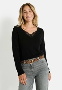 Haut noir à manches longues avec un décolleté en V, orné de dentelle. Associé à un jean gris et une ceinture brune à imprimé léopard.
