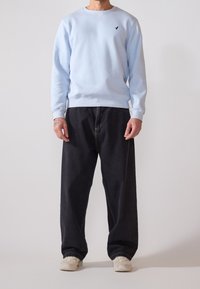 Felpa azzurra chiara con maniche lunghe, colletto rotondo e un piccolo logo nero sul petto, abbinata a un paio di jeans in denim scuro a gamba larga.
