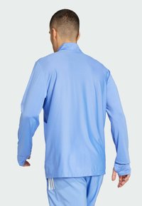 Light blue athletic jacket made of breathable fabric, featuring long sleeves and thumbholes, designed for comfort and mobility.