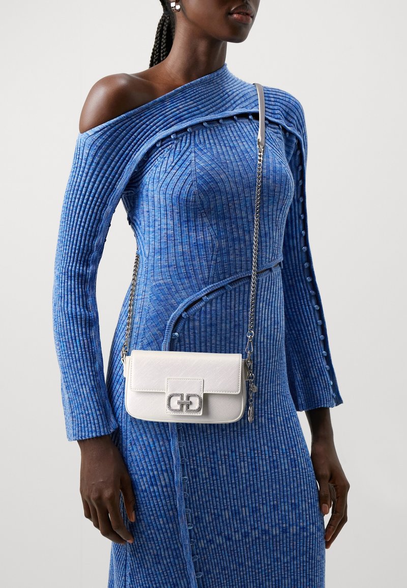 Blaumes geripptes Kleid mit asymmetrischem Ausschnitt und Knopfdetails, kombiniert mit einer kleinen weißen Leder-Umhängetasche mit silberner Verzierung.