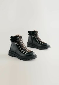Bottes de randonnée en cuir noir avec une semelle en caoutchouc robuste, dotées de crochets métalliques pour les lacets et d'une doublure en fausse fourrure confortable. La fermeture éclair latérale ajoute de la commodité.