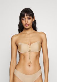 Soutien-gorge nude sans bretelles en tissu lisse, avec des bonnets en forme de cœur et un système de laçage à l'avant. Compressé sur les bords pour un aspect sans couture.