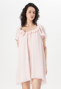 Šviesiai rožinė be rankovių suknelė, pagaminta iš minkštos, permatomos medžiagos. Suknelė turi volangų apykaklę ir rankogalius, o kairėje pusėje yra gėlių akcentas.