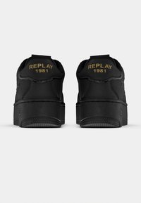 Ζευγάρι μαύρα αθλητικά παπούτσια, φωτογραφημένα από πίσω, με χοντρές σόλες και το «REPLAY 1981» σε χρυσά γράμματα στις πίσω ετικέτες.