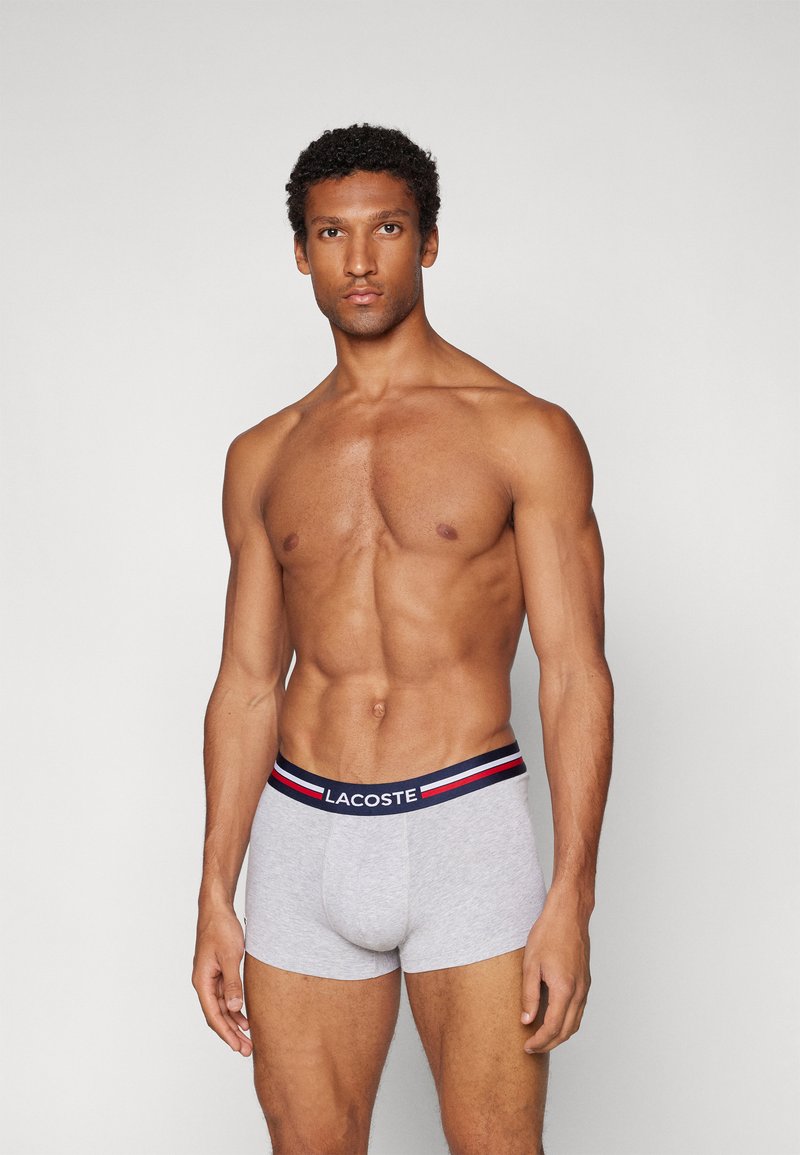 Boxer-briefs pour hommes en coton gris avec une taille noire ornée de rayures rouges et bleues ; coupe ajustée avec une poche avant pour le soutien.