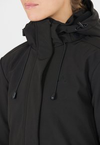 Sort softshell jakke med høj krave og justerbare snore, prydet med et diskret logo og en tekstureret overflade.