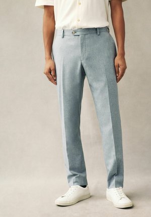 Helle blaue Hose aus strukturiertem Stoff, schmaler Schnitt, seitliche Streifen und vorn mit Knopfverschluss, kombiniert mit weißen Sneakers.