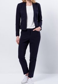 Námořnický blazer a odpovídající kalhoty vyrobené z tkané látky, spárované s bílým topem. Blazer má úzký střih, zatímco kalhoty mají zúžený design.