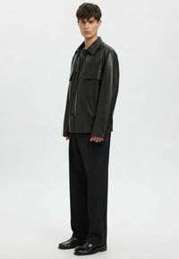 Must nahast jakk krae ja ees nuppudega sulgemisega ning kahe rinnataskuga. Kanditud mustade kohandatud pükste ja mustade kingadega.