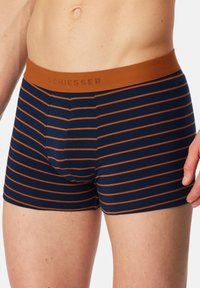 Marineblauwe boxershorts met horizontale oranje strepen, een bruine elastische tailleband met het label "SCHIESSER", gemaakt van een zachte stof.