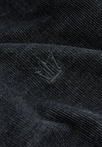 Tessuto di cotone nero con una trama sottile e testurizzata. Presenta un piccolo logo di corona ricamato con filo nero coordinato.