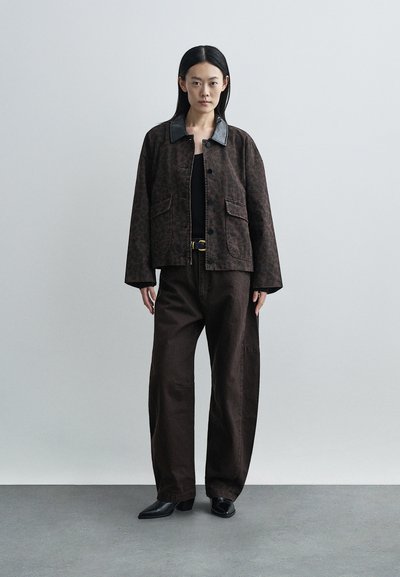 Jachetă maro cu imprimeu leopard, guler negru, două buzunare frontale și croială lejeră, asortată cu pantaloni maro largi și cizme negre până la gleznă.