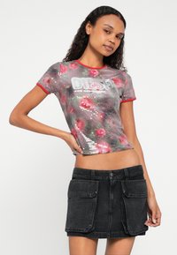 Priliehavý krátky rukáv s flitrovým kvetinovým vzorom v odtieňoch ružovej a zelenej, ohraničený červeným výstrihom, v kombinácii s čiernou rifľovou sukňou.