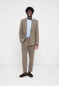 Beige double-breasted suit with a light blue dress shirt and brown loafers. The suit features subtle stitching and a notched lapel.
