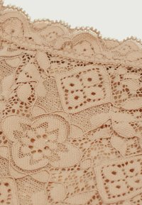 Lace stof in een zachte perziktint met ingewikkelde bloempatronen en gegolfde randen, die het delicate opengewerkte textuur accentueert.
