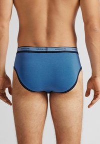 Blaue Baumwollslips mit Marineblauen Akzenten und einem elastischen Bund, der den Markennamen trägt. Glatte Textur und enganliegende Passform.