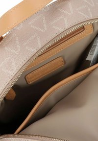 Interior de bolso beige con cremallera y logo, con una textura suave y dos compartimentos. Forrado con tela rosa claro que muestra un patrón de logo.