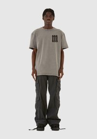 Grå oversized t-skjorte med svart "m"-logo på brystet, kombinert med løs passform svarte cargo-bukser med flere lommer og snøring på kantene.