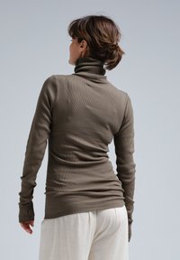 Brauner gerippter Rollkragenpullover mit langen Ärmeln, figurbetonter Schnitt, mit Daumenlöchern an den Bündchen und einer glatten Textur. Der Hintergrund ist hellgrau.
