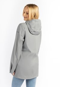 Giacca impermeabile grigia chiara con cappuccio, maniche lunghe e un design elegante. Presenta una texture liscia e polsini regolabili.