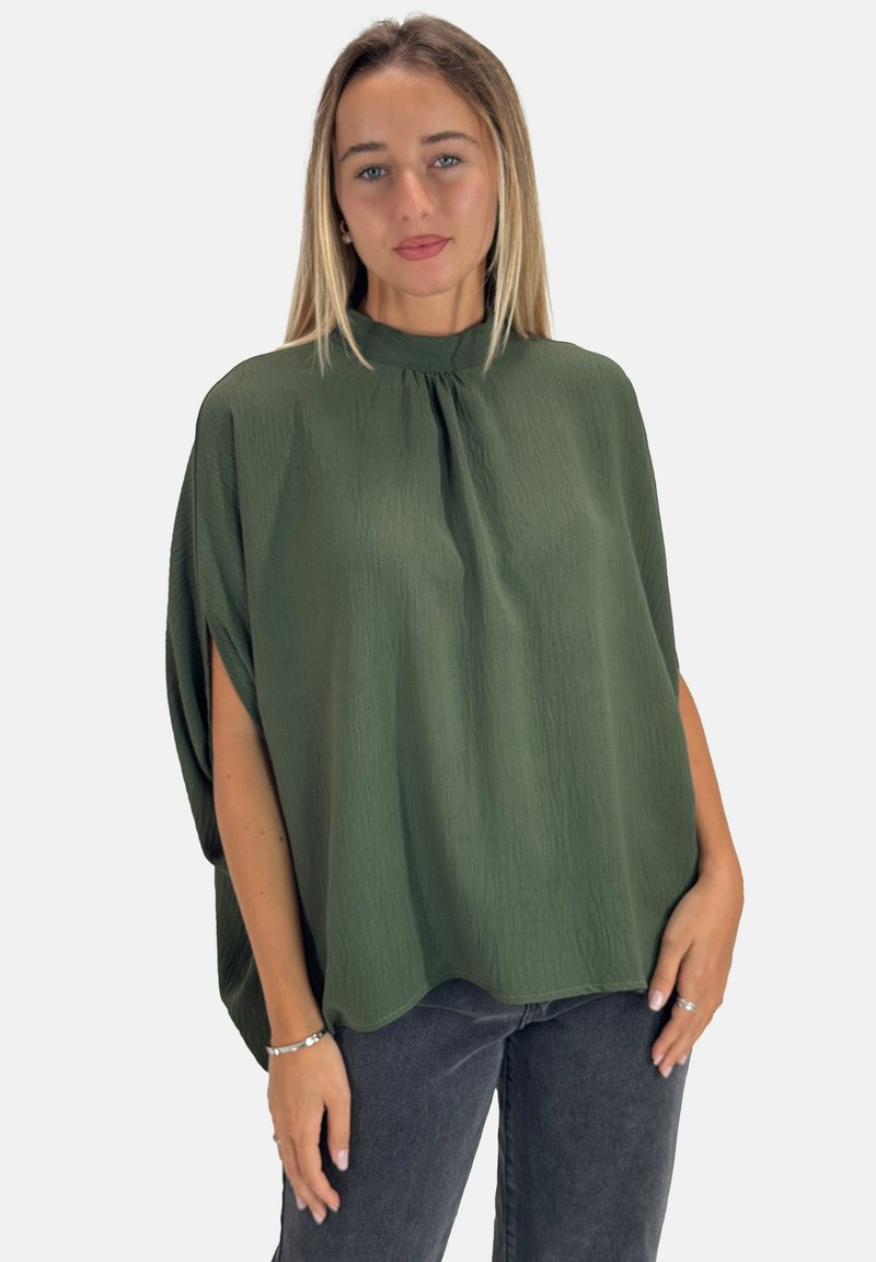 Grøn, tekstureret ponchostil top med høj hals og løs pasform, med brede ærmer, kombineret med mørke jeans.