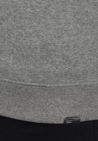 Grauer Sweatshirt mit geripptem Saum und Bündchen, aus weichem, strukturiertem Fabric, mit einem kleinen Logo-Tag nahe dem Saum.