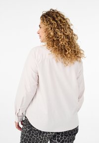 Hellrosa langärmliges Hemd mit abgerundetem Saum und knöpfbaren Manschetten, kombiniert mit schwarzer und grauer Leopardenmuster-Hose. Weicher Stoff.