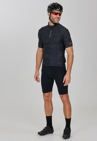 Zwarte fietsjersey met korte mouwen, volledige rits en bijpassende zwarte shorts. Draag het met een zwarte helm en een zonnebril.