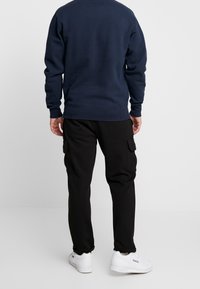 Sudadera azul marino con puños acanalados, combinada con pantalones cargo negros que cuentan con bolsillos laterales. Zapatillas blancas completan el atuendo.