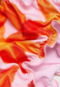 Kopalke s tie-dye vzorom v roza in oranžnih odtenkih, z nabranimi robovi in mehko, raztegljivo teksturo tkanine.